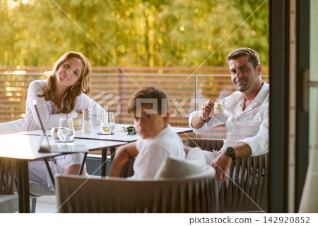 Family Relaxing On Balcony Terrace Together Having Coffee And Conversation In Warm Sunset Light 142920852