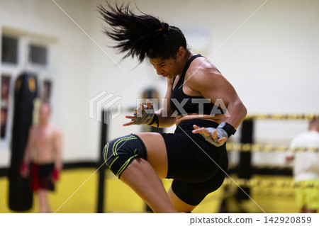 Female MMA Fighter Performing A Powerful Jump Kick During Intense Gym Training Session Female MMA Fighter Performing A Powerful Jump Kick During Intense Gym Training Session 142920859
