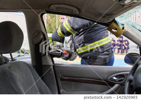 Firefighter Performing Vehicle Extrication With Hydraulic Cutter During Emergency Rescue Training Drill Firefighter Performing Vehicle Extrication With Hydraulic Cutter During Emergency Rescue Training Drill 142920965