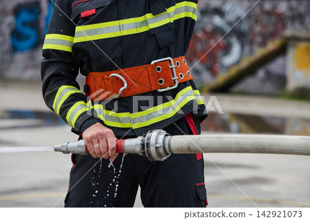 Firefighter Holding Hose in Turnout Gear Spraying Water During Urban Training Exercise 142921073
