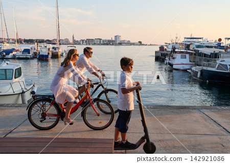 Family Cycling and Electric Scooter By The Harbor At Sunset During Summer Vacation 142921086