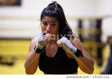 Female Boxer Training in Boxing Gym Ringside Punching With Wrapped Hands and Determined Expression Female Boxer Training in Boxing Gym Ringside Punching With Wrapped Hands and Determined Expression 142921122