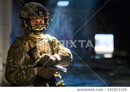 Armed Soldier in Camouflage Gear Standing in Dim Urban Building With Tactical Rifle and Helmet Armed Soldier in Camouflage Gear Standing in Dim Urban Building With Tactical Rifle and Helmet 142921326