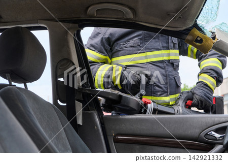 Firefighter Performing Vehicle Extrication With Hydraulic Rescue Tool At Car Accident Scene Firefighter Performing Vehicle Extrication With Hydraulic Rescue Tool At Car Accident Scene 142921332