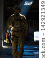 Tactical Soldier in Camouflage Gear With Rifle Walking Through Abandoned Urban Building Bathed in Light 142921349