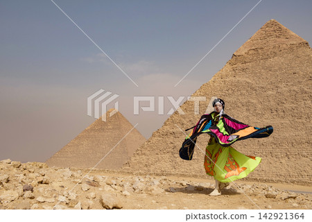 Whirling performer caught mid spin with a dramatic billowing multicolor patchwork cape against the iconic Giza Pyramids on the desert plateau in bold Whirling performer caught mid spin with a dramatic billowing multicolor patchwork cape against the iconic Giza Pyramids on the desert plateau in bold 142921364