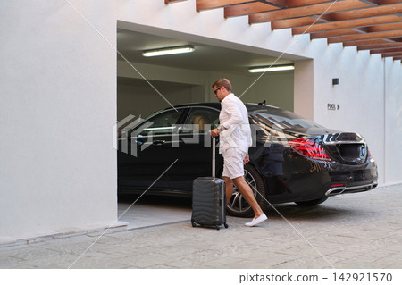 Man With Luggage Walking to Luxury Car in Resort Garage Near Pool on Vacation Man With Luggage Walking to Luxury Car in Resort Garage Near Pool on Vacation 142921570