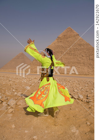 Whirling dervish performer in vibrant neon yellow orange embroidered robe spinning with arms raised before iconic Great Pyramids of Giza Egypt ideal Whirling dervish performer in vibrant neon yellow orange embroidered robe spinning with arms raised before iconic Great Pyramids of Giza Egypt ideal 142921670