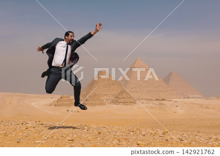 Exhilarated arab businessman leaping mid air in suit at Giza Pyramids Egypt ideal for global business success travel and MENA campaigns Exhilarated arab businessman leaping mid air in suit at Giza Pyramids Egypt ideal for global business success travel and MENA campaigns 142921762