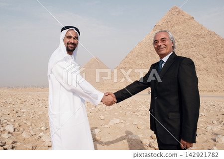 Cross cultural business handshake between Arab executive in thobe and senior Western professional before Giza Pyramids Egypt desert Cross cultural business handshake between Arab executive in thobe and senior Western professional before Giza Pyramids Egypt desert 142921782