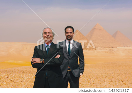 Two arab executives multigenerational business duo standing with confidence before iconic Giza Pyramids on sunlit Egyptian desert plateau ideal for Two arab executives multigenerational business duo standing with confidence before iconic Giza Pyramids on sunlit Egyptian desert plateau ideal for 142921817