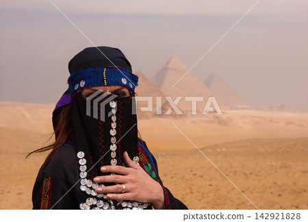 Proud niqab portrait of woman wearing ornate coin adorned traditional arabic costume with embroidered robe standing before the iconic Giza Pyramids in Proud niqab portrait of woman wearing ornate coin adorned traditional arabic costume with embroidered robe standing before the iconic Giza Pyramids in 142921828