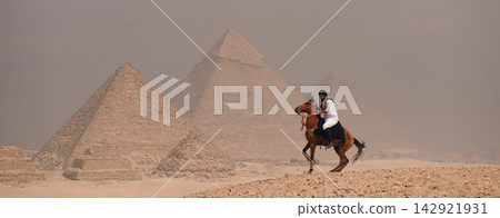 Arab horseman on galloping horse near Great Pyramids of Giza dramatic desert haze Egypt travel and heritage Arab horseman on galloping horse near Great Pyramids of Giza dramatic desert haze Egypt travel and heritage 142921931