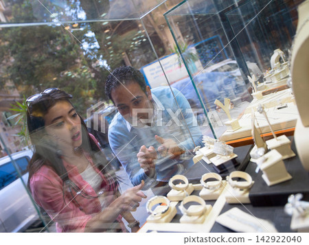 Couple browsing engagement rings in a jewelry store window display choosing a luxury gift together Couple browsing engagement rings in a jewelry store window display choosing a luxury gift together 142922040