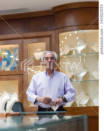 Jeweler shop owner counting cash behind glass counter in upscale jewelry boutique portrait Jeweler shop owner counting cash behind glass counter in upscale jewelry boutique portrait 142922053