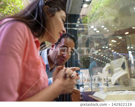 Couple admiring jewelry in a store window display while window shopping together Couple admiring jewelry in a store window display while window shopping together 142922119