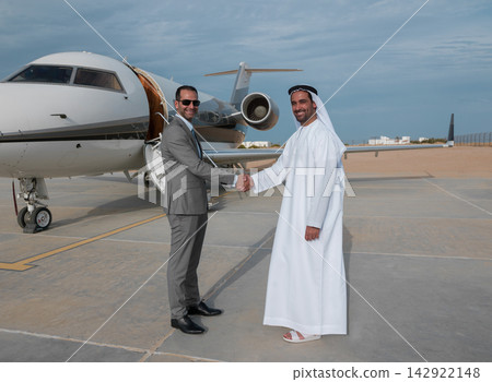 Middle Eastern business partners shaking hands in front of a private jet on the tarmac Middle Eastern business partners shaking hands in front of a private jet on the tarmac 142922148