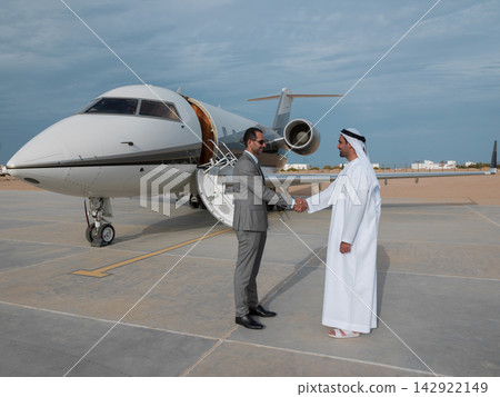 Middle Eastern business partners shake hands beside private jet on airport tarmac celebrating deal Middle Eastern business partners shake hands beside private jet on airport tarmac celebrating deal 142922149