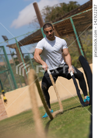 Athletic man doing outdoor battle ropes workout at a fitness training facility on a sunny day Athletic man doing outdoor battle ropes workout at a fitness training facility on a sunny day 142922287
