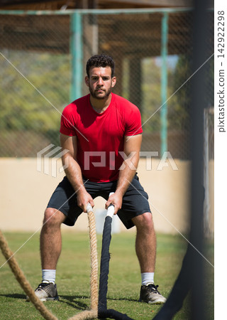 Young man doing outdoor CrossFit rope workout showing strength, focus and athletic training Young man doing outdoor CrossFit rope workout showing strength, focus and athletic training 142922298