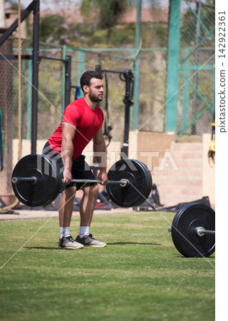 Middle Eastern man doing heavy deadlift at outdoor CrossFit gym in red shirt Middle Eastern man doing heavy deadlift at outdoor CrossFit gym in red shirt 142922361