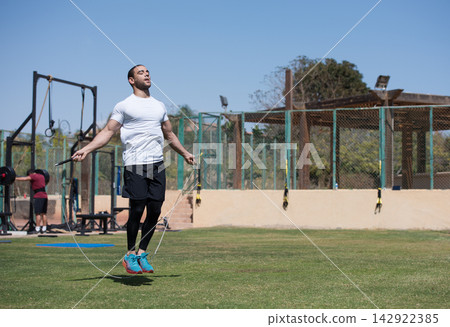 Middle Eastern man jumping rope during outdoor CrossFit workout at open-air fitness gym with friend 142922385
