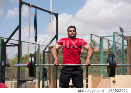 Middle Eastern man performing CrossFit barbell lift in outdoor gym with friend during strength training Middle Eastern man performing CrossFit barbell lift in outdoor gym with friend during strength training 142922431
