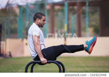 Man doing L-sit calisthenics on parallel bars during outdoor crossfit fitness workout with a friend Man doing L-sit calisthenics on parallel bars during outdoor crossfit fitness workout with a friend 142922446