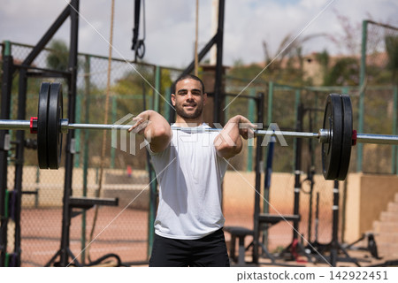 Man lifting barbell at outdoor CrossFit gym during strength training with a workout partner Man lifting barbell at outdoor CrossFit gym during strength training with a workout partner 142922451