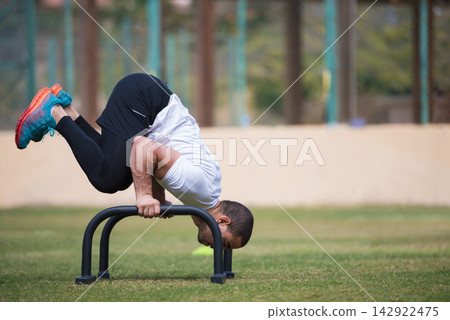 Outdoor fitness workout: man performing advanced CrossFit bodyweight exercise on parallette bars Outdoor fitness workout: man performing advanced CrossFit bodyweight exercise on parallette bars 142922475