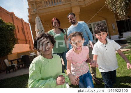Happy Middle Eastern Arab family playing together with parents and children in a backyard Happy Middle Eastern Arab family playing together with parents and children in a backyard 142922500