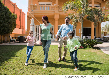 Happy family walking and playing together in a sunny villa garden holding hands Happy family walking and playing together in a sunny villa garden holding hands 142922555