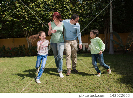 Modern Middle Eastern family walking and laughing together in sunny backyard playing with children Modern Middle Eastern family walking and laughing together in sunny backyard playing with children 142922663