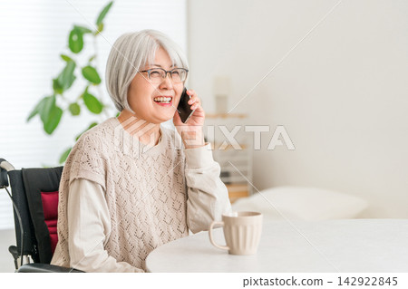 一位坐在輪椅上的老婦人正津津有味地用智慧型手機通話。一位頭髮花白的老人在打電話時面帶微笑。 一位坐在輪椅上的老婦人正津津有味地用智慧型手機通話。一位頭髮花白的老人在打電話時面帶微笑。 142922845
