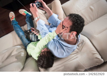 Middle Eastern father and son playing video games together on couch during Eid Ramadan family gathering 142922920