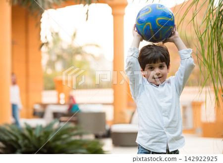 Young boy playing with a soccer ball at a modern Middle Eastern family home during Eid gathering 142922925