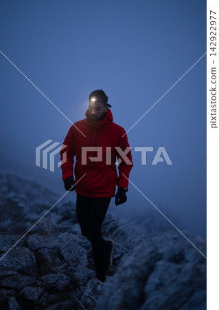 Hiker Wearing Red Jacket And Headlamp Walking On Rocky Mountain Trail At Dusk In Fog Hiker Wearing Red Jacket And Headlamp Walking On Rocky Mountain Trail At Dusk In Fog 142922977
