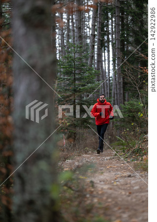 Trail Running In Forest With Male Runner Wearing Red Jacket During Outdoor Fitness Session 142922986