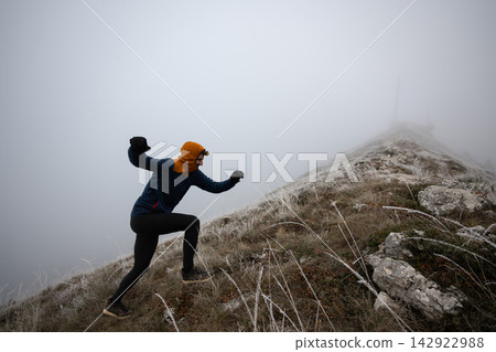 Trail Runner Hiking Up Frosty Mountain Ridge In Thick Fog Wearing Winter Running Gear Trail Runner Hiking Up Frosty Mountain Ridge In Thick Fog Wearing Winter Running Gear 142922988