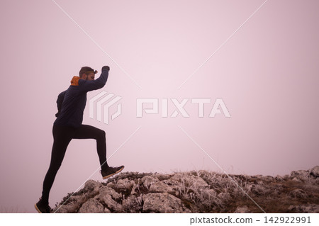 Man Hiking Up Rocky Ridge Into Misty Pink Sky Outdoor Fitness Adventure and Determination 142922991