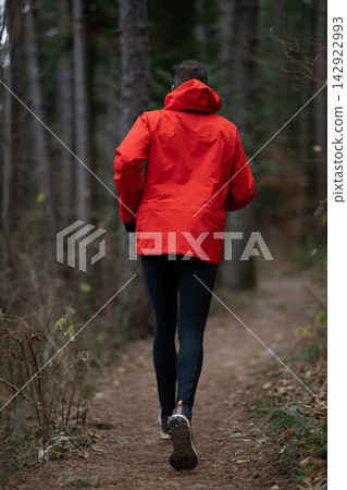 Trail Runner In Red Jacket Jogging Through Forest Path For Outdoor Fitness And Winter Training 142922993