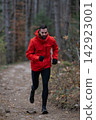 Bearded Man Running on Forest Trail in Red Jacket During Autumn Outdoor Fitness Training 142923001