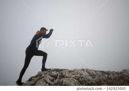 Trail Runner Climbing Foggy Mountain Ridge at Dawn Wearing Headlamp and Cold-Weather Gear Trail Runner Climbing Foggy Mountain Ridge at Dawn Wearing Headlamp and Cold-Weather Gear 142923005
