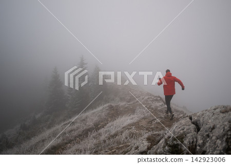 Trail Runner In Red Jacket Running Along Foggy Mountain Ridge In Frosty Winter Landscape Trail Runner In Red Jacket Running Along Foggy Mountain Ridge In Frosty Winter Landscape 142923006