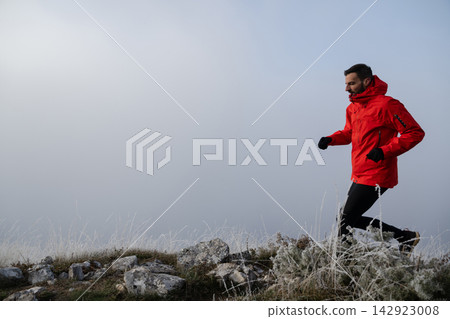 Man Trail Running in Red Jacket on Frosty Mountain Ridge During Cold Overcast Morning 142923008