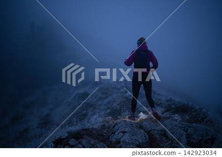 Female Trail Runner On Foggy Mountain Ridge At Dusk With Headlamp And Winter Jacket Female Trail Runner On Foggy Mountain Ridge At Dusk With Headlamp And Winter Jacket 142923034