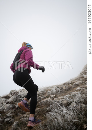 Woman Hiking Uphill on Frosty Mountain Trail in Winter Gear for Outdoor Fitness Adventure 142923045