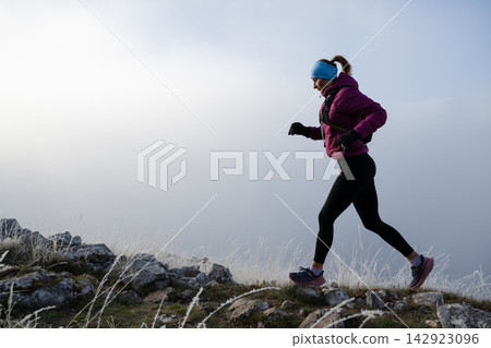 Woman Trail Running on Frosty Mountain Ridge Wearing Winter Running Gear at Sunrise Woman Trail Running on Frosty Mountain Ridge Wearing Winter Running Gear at Sunrise 142923096