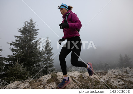 Woman Trail Runner Wearing Headlamp Running on Rocky Mountain Trail in Foggy Winter Morning for Fitness Woman Trail Runner Wearing Headlamp Running on Rocky Mountain Trail in Foggy Winter Morning for Fitness 142923098