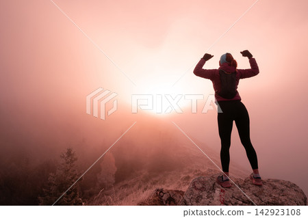 Female Hiker Celebrating Sunrise On Mountain Summit, Silhouette Above Misty Forest And Cliff Female Hiker Celebrating Sunrise On Mountain Summit, Silhouette Above Misty Forest And Cliff 142923108